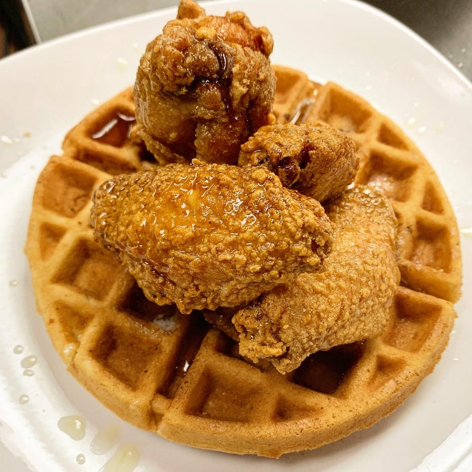 Golden-brown fried chicken pieces drizzled with syrup, served atop a waffle on a white plate.