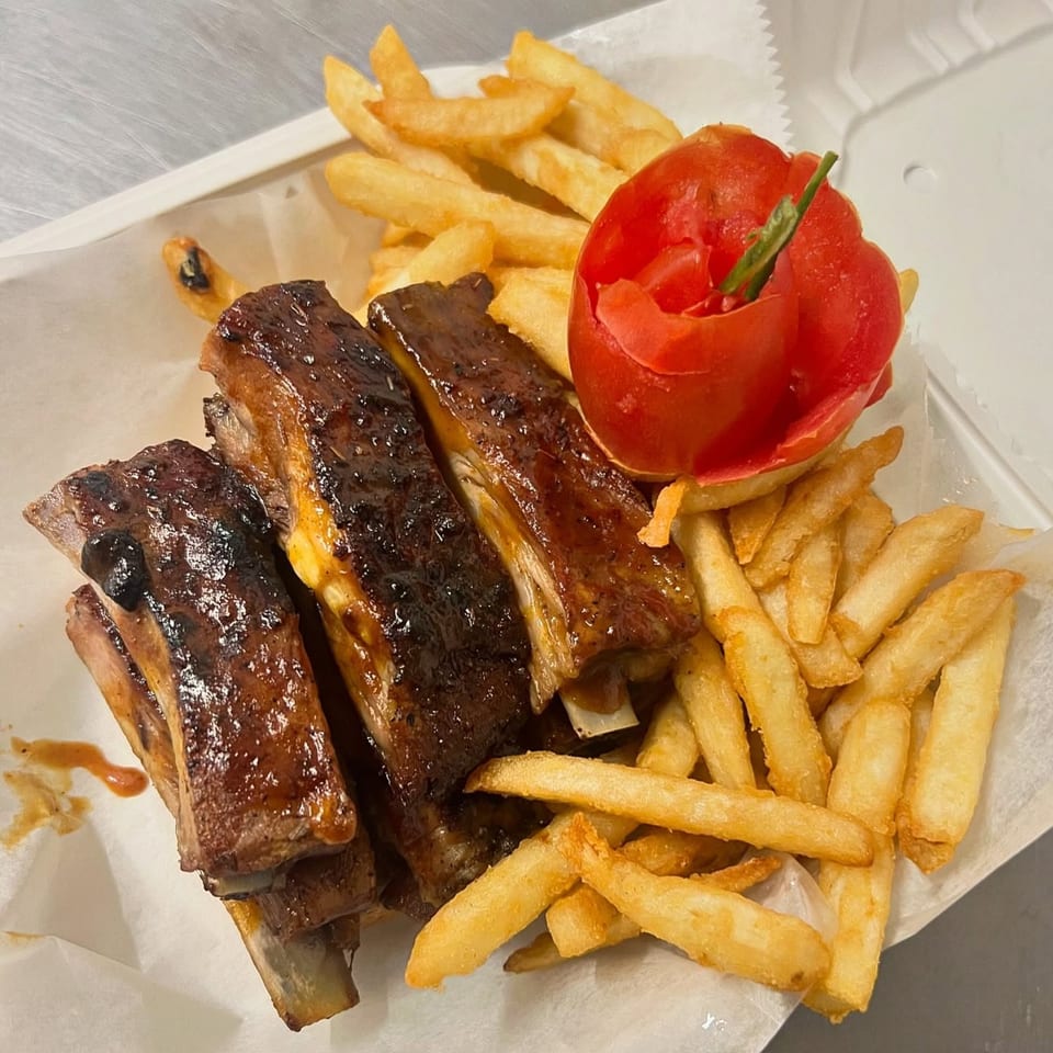Fireman's Cafe BBQ ribs with french fries and a carved tomato garnish in a white container.