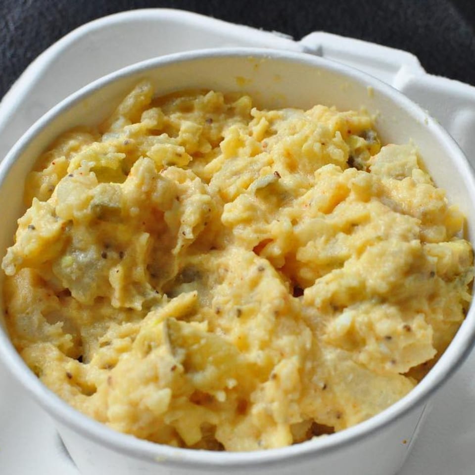 A white cup filled with creamy, yellow potato salad, speckled with black pepper, from Fireman's Cafe.