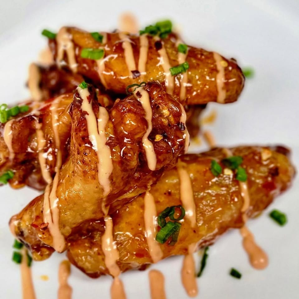 Crispy Fireman's Cafe chicken wings drizzled with sauce and garnished with green onions on a white plate.