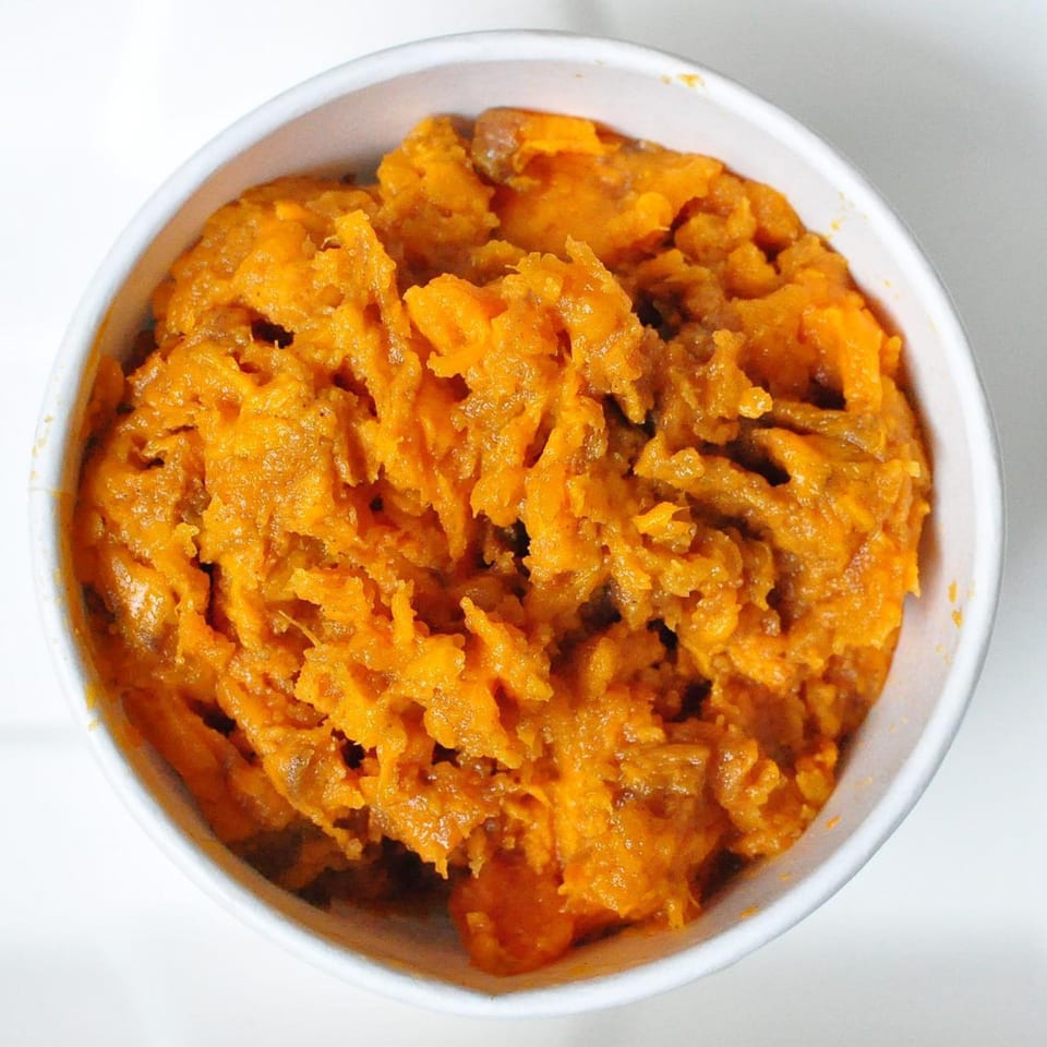 Close-up overhead view of a white bowl filled with bright orange mashed sweet potatoes.