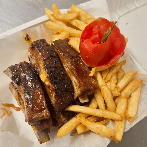 Fireman's Cafe BBQ ribs with french fries and a carved tomato in a takeout container.